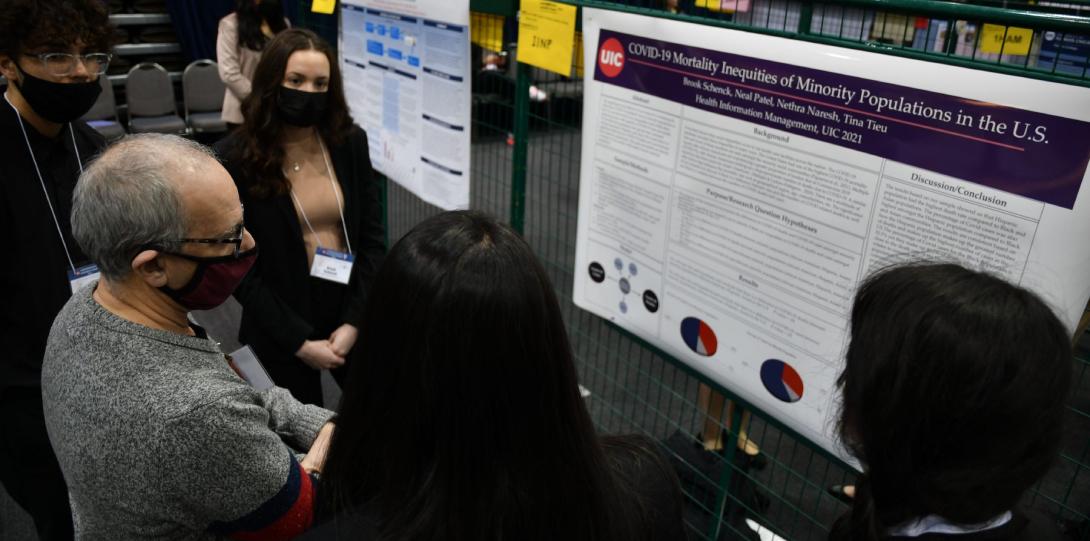 A student presents their research to several attendees at the 2022 Undergraduate Research Forum